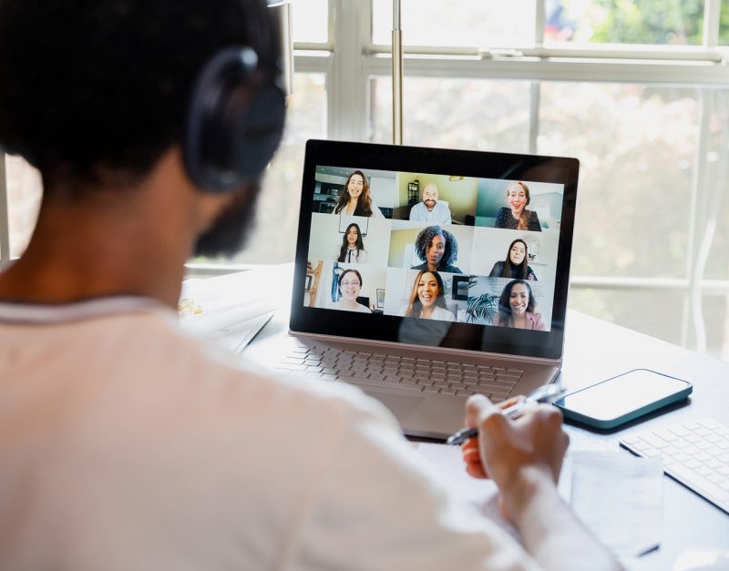An over-the-shoulder view of an unrecognizable university student meeting online with his teacher and fellow students.