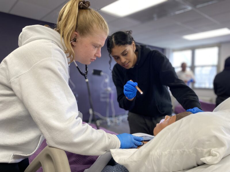 two female nurse students checking pulse on doll