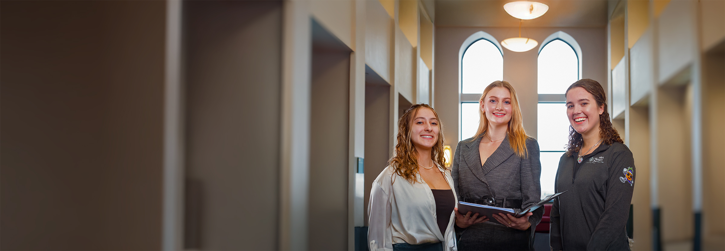 Three students in the college of hospitality offices with one of them holding a folder