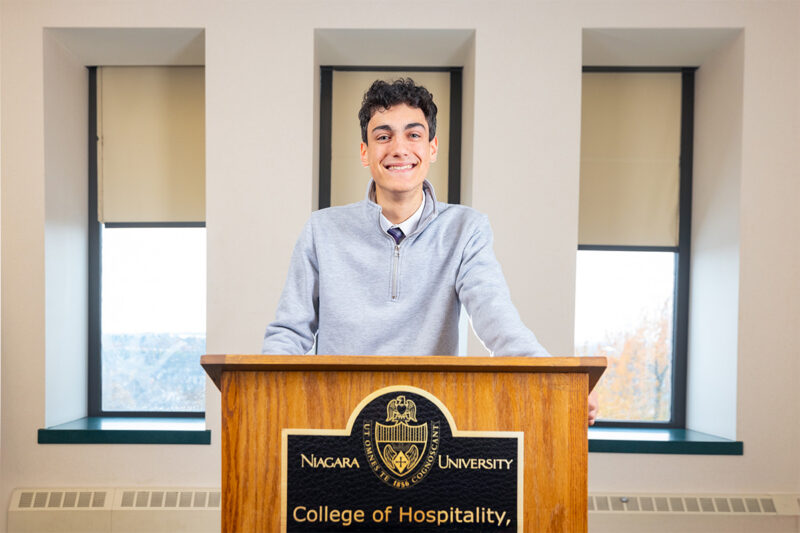 Student from the college of hospitality smiling and standing in front of a lectern.