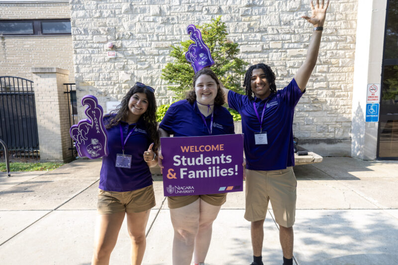 Orientation leaders holding welcome students and families sign