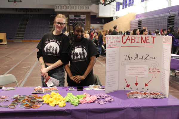 Students at a table that contains rubber bracelets, pamphlets and a poster