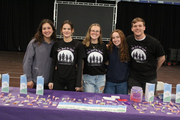 Students standing behind a table that contains stickers, suckers and pamphlets