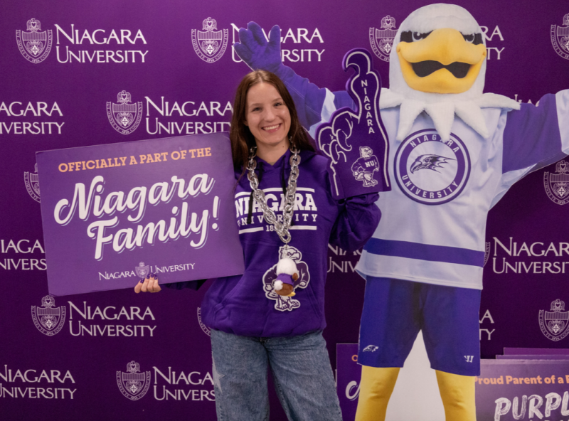Incoming NU student holding a niagara family sign next to a cardboard cutout of Monte