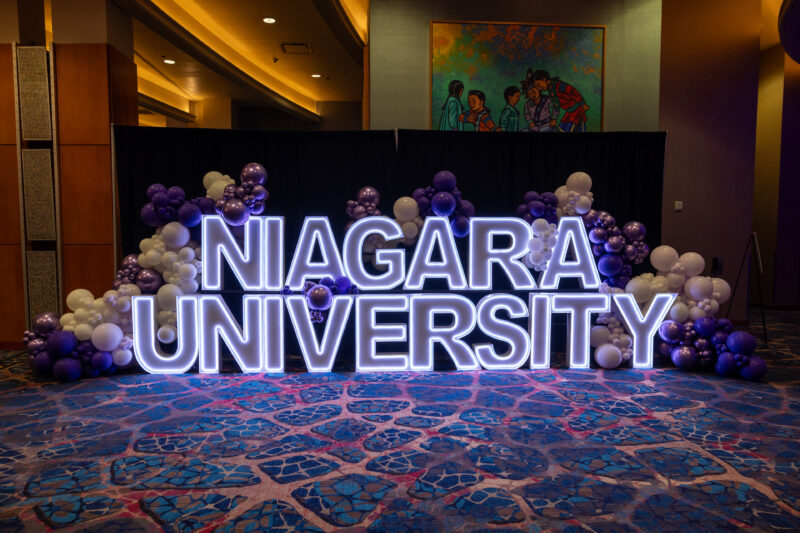 Niagara University letters in lights surrounded by white and purple balloons