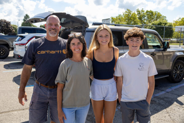 Student with parents and sibling standing in front of a car in the seton parking lot