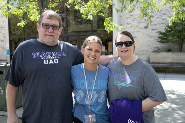Student with parents standing in fromt of a tree outside of gally